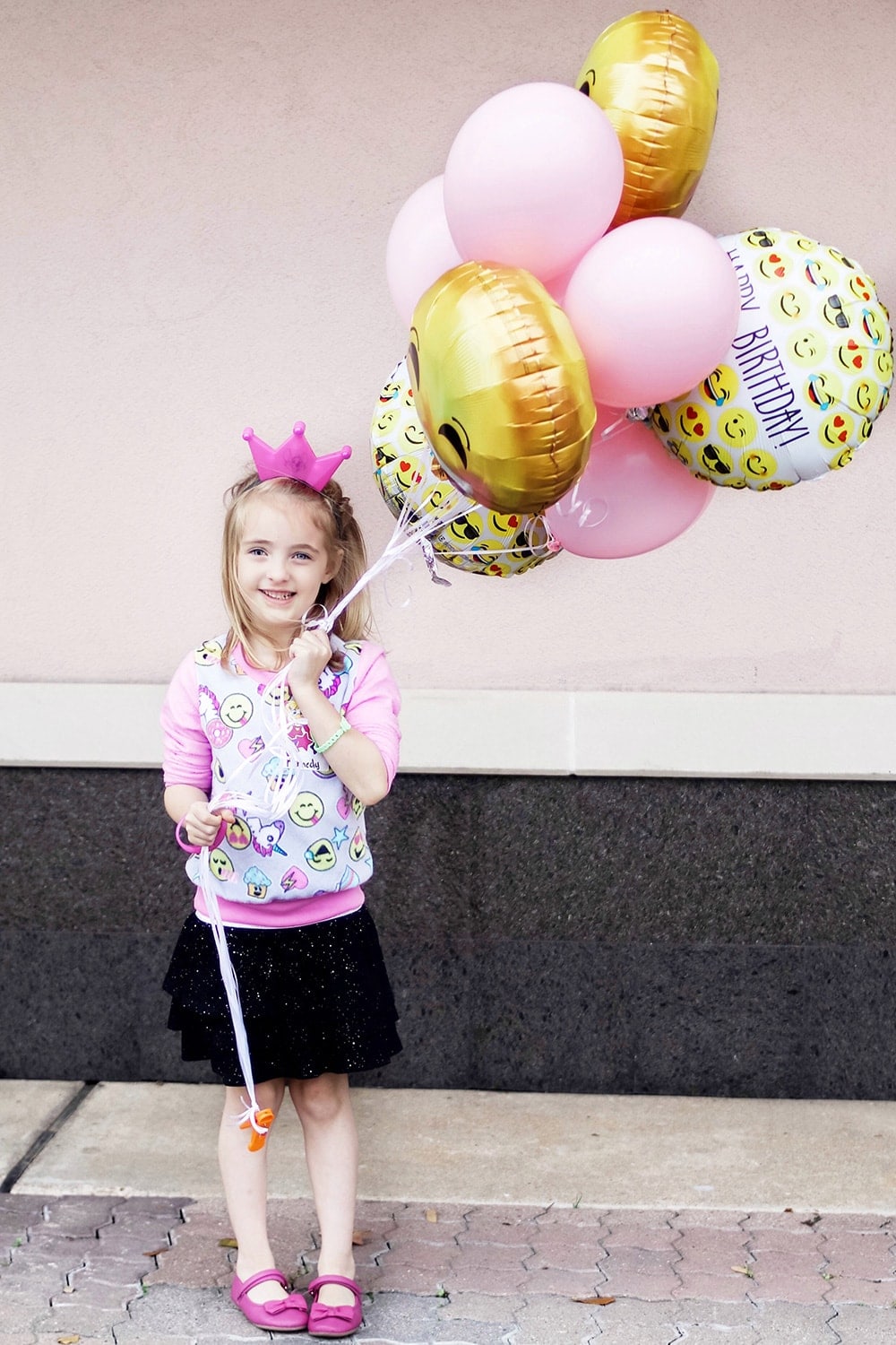birthday girl holding pink and emoji balloons